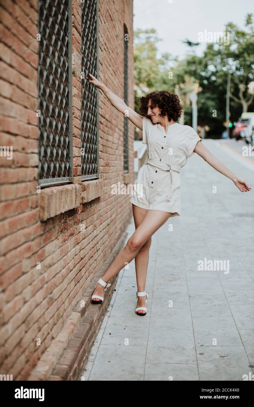 Donna mid adulta con le braccia tese in piedi su strada vicino muro di mattoni in città Foto Stock