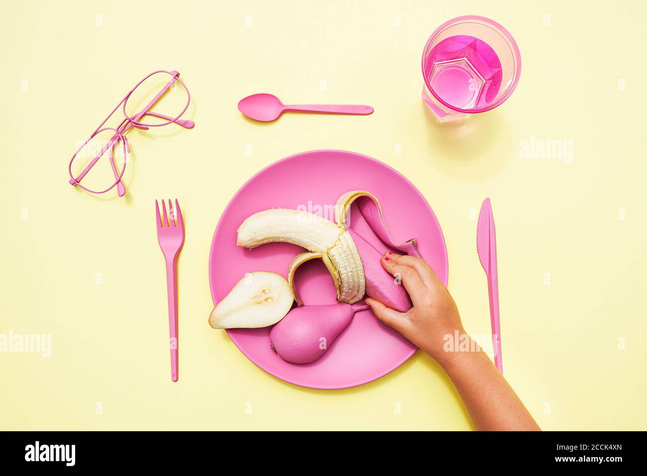 Mano della bambina che raccoglie la banana rosa-colorata dalla plastica piastra Foto Stock
