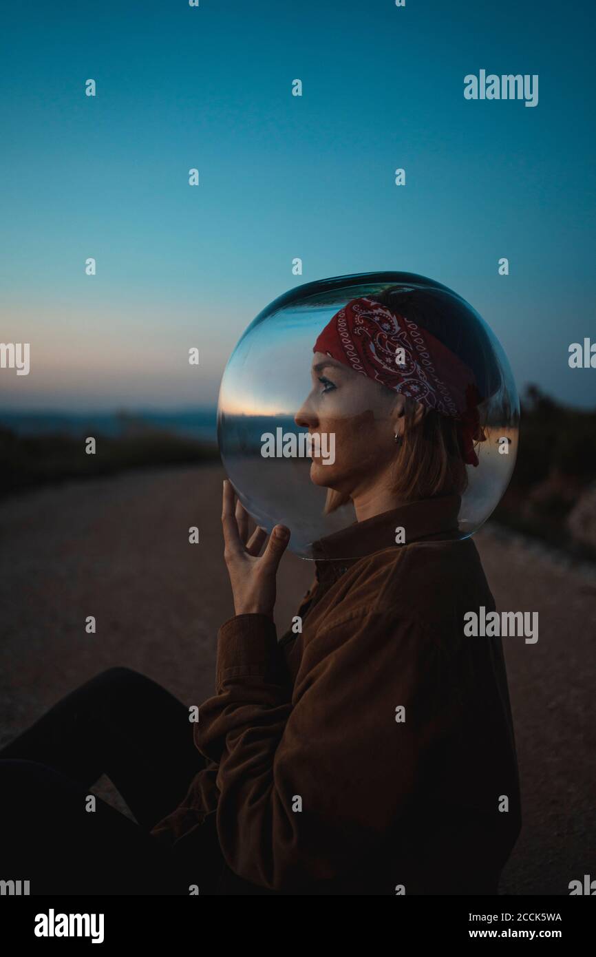Donna con una ciotola di pesce sulla testa seduta una strada in campagna al tramonto Foto Stock
