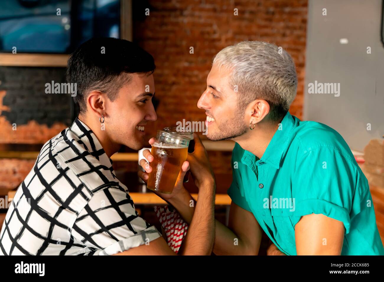 Romantica coppia gay gustando la birra con il braccio in braccio al bar Foto Stock