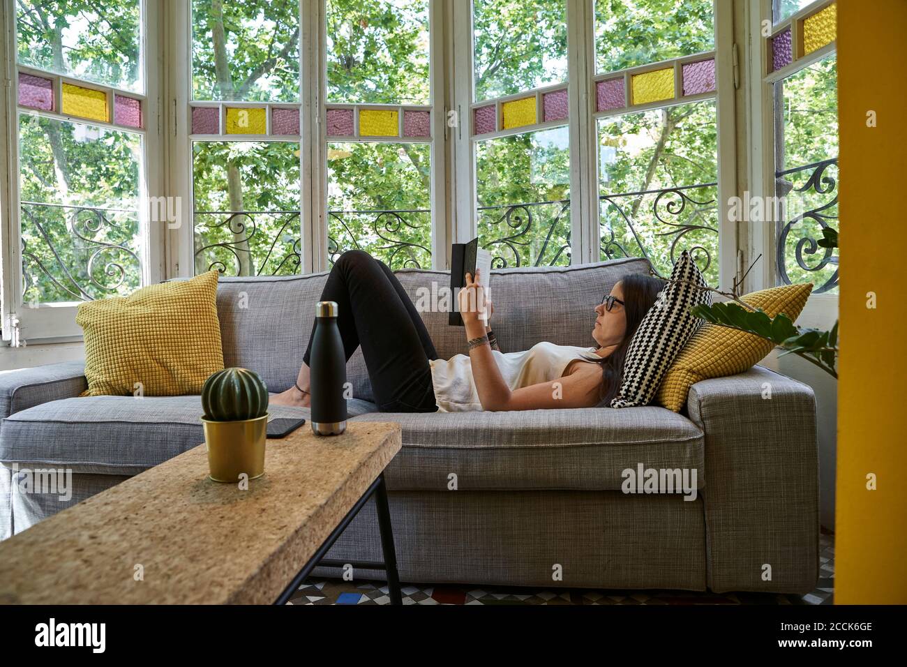 Donna che legge libro mentre si rilassa sul divano in soggiorno Foto Stock
