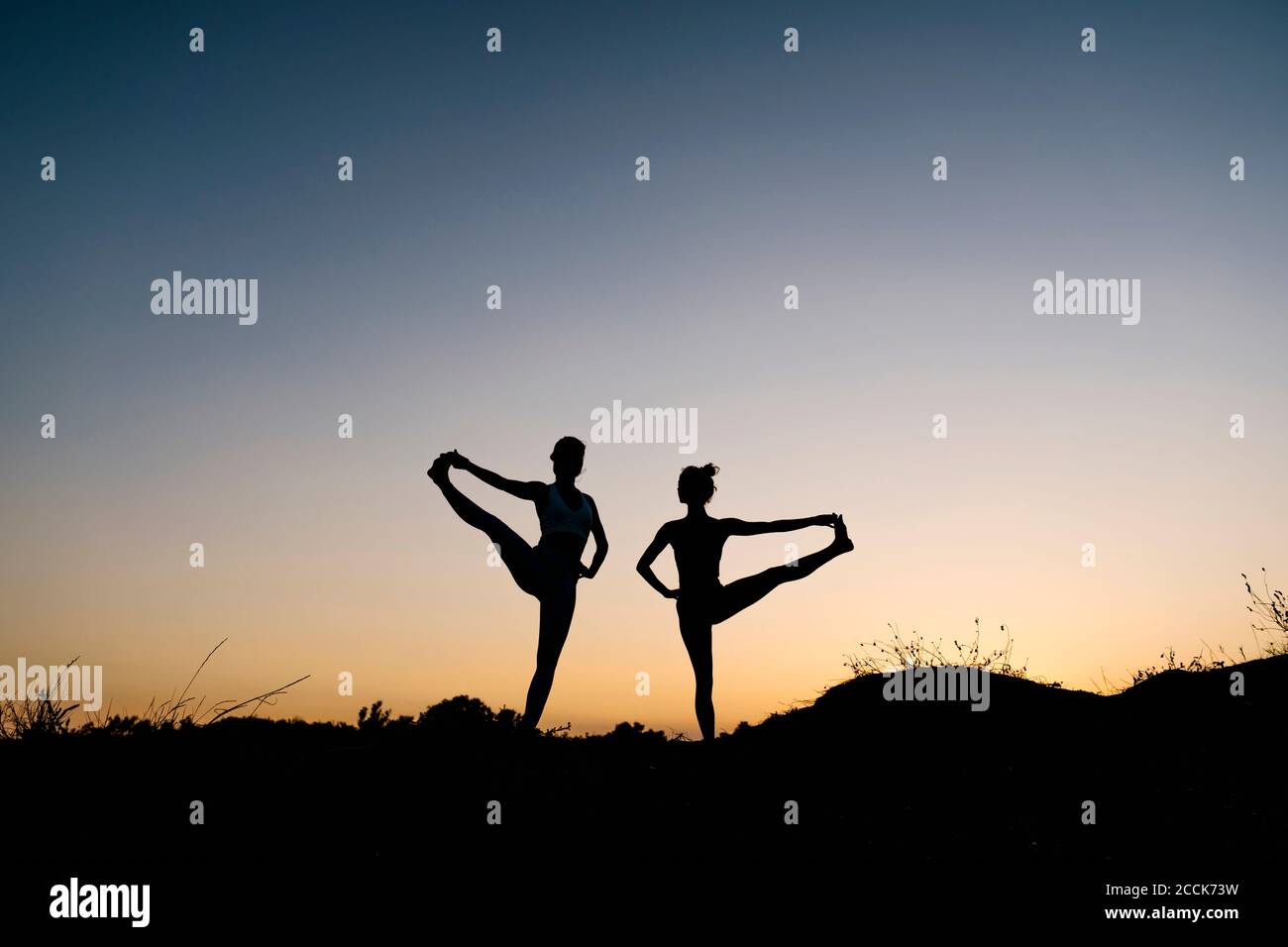 Silhouette donne che praticano la mano al piede grande posa contro chiaro cielo Foto Stock