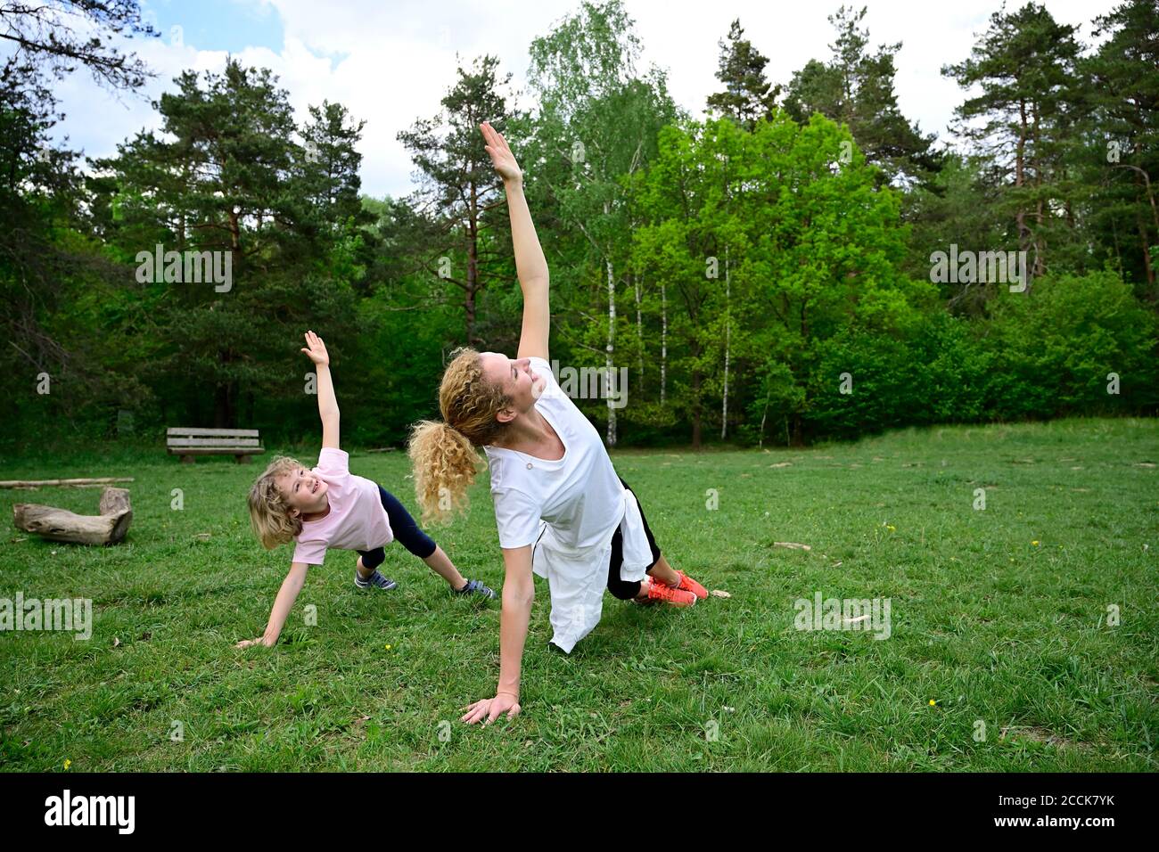 Madre e figlia che praticano la tavola laterale posa su terra erbosa in foresta Foto Stock