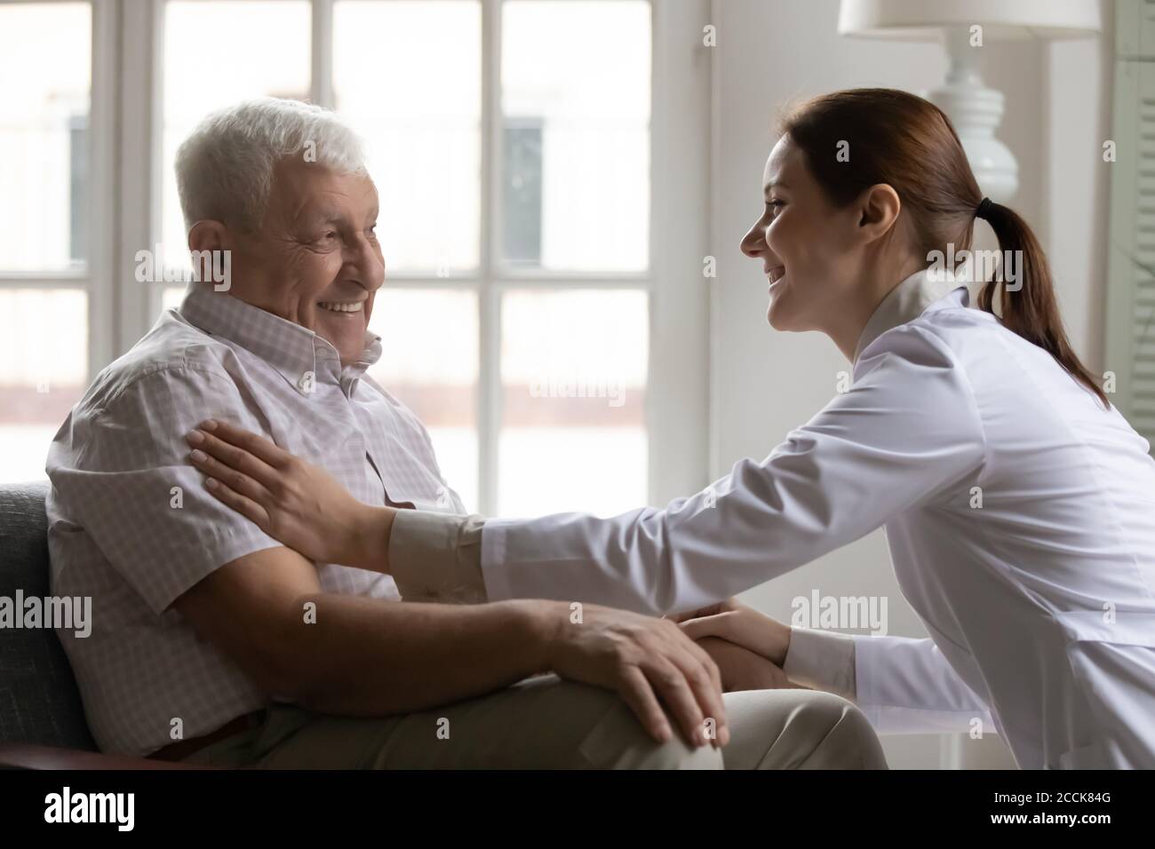 Sorridente giovane donna gentile dottore che sostiene felice anziano anni 80 paziente. Foto Stock
