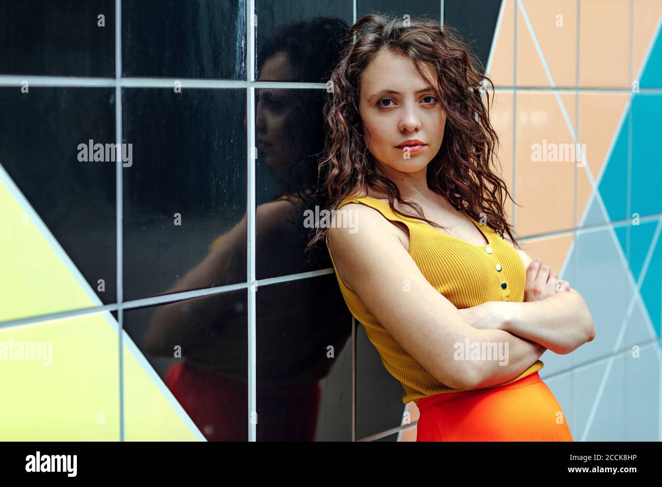 Giovane donna con braccia incrociate appoggiate su colorate pareti piastrellate Foto Stock
