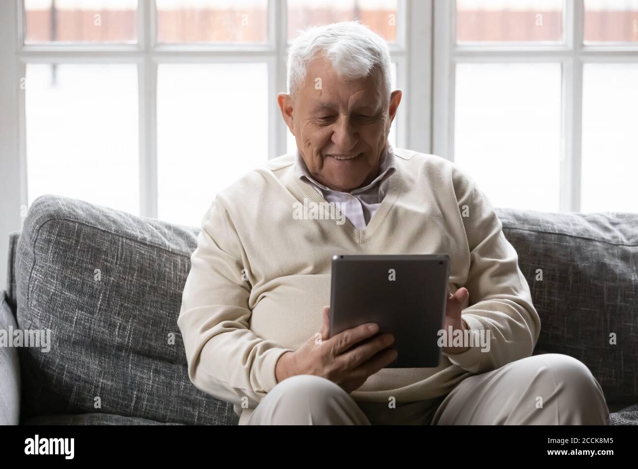 Sorridi un anziano pensionato maschile utilizzando un tablet per computer digitale. Foto Stock