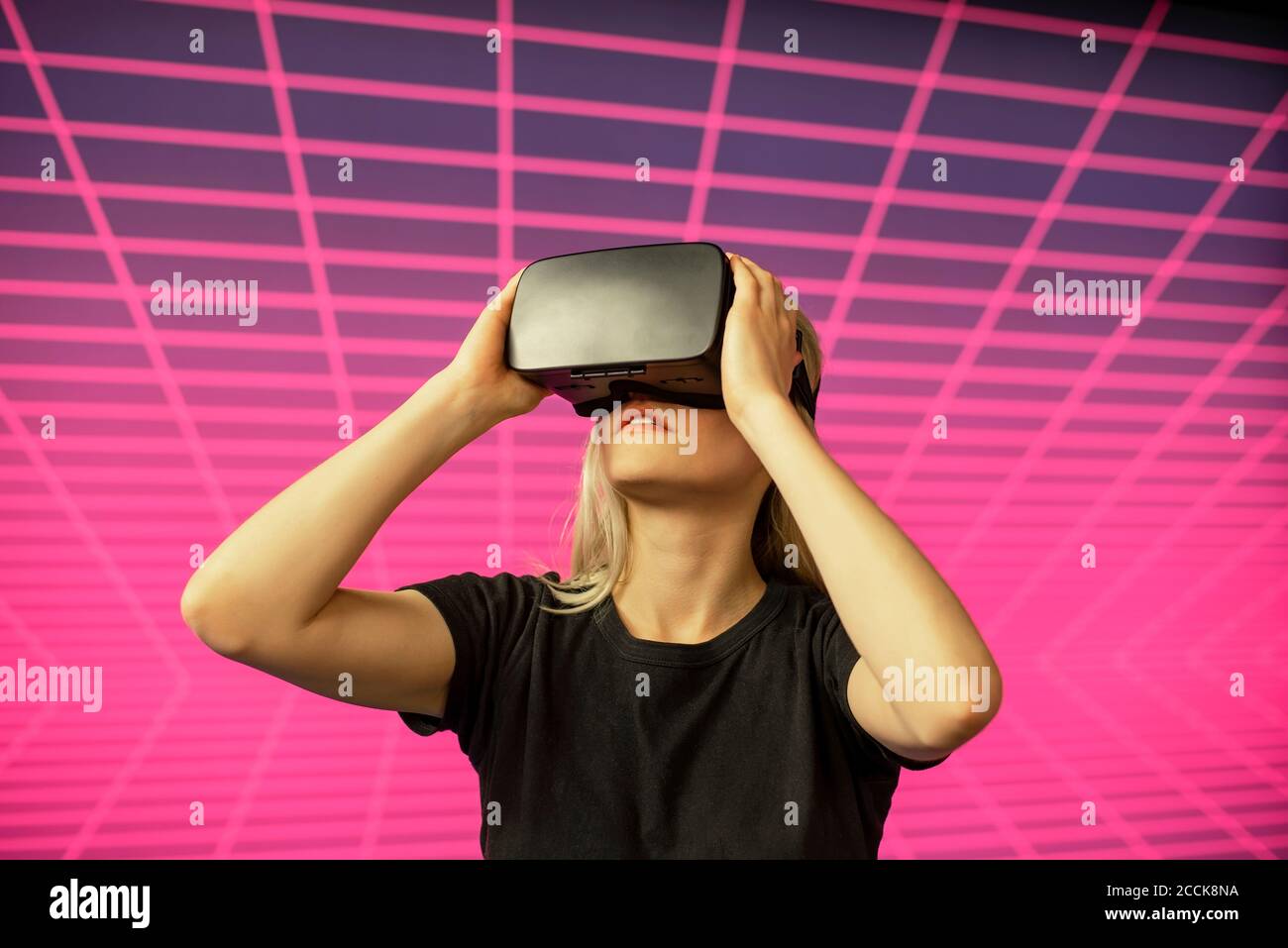 Scienziato femminile che guarda attraverso il simulatore di realtà virtuale contro il modello di griglia Foto Stock