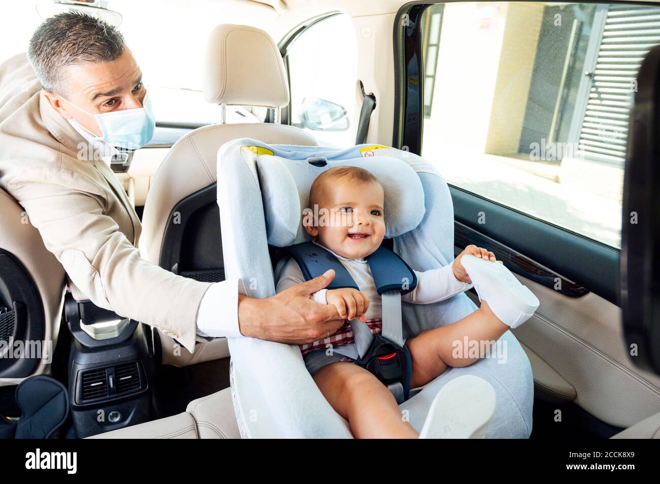 Padre che indossa una maschera protettiva bambino ragazzo seduto sul seggiolino del bambino in auto Foto Stock