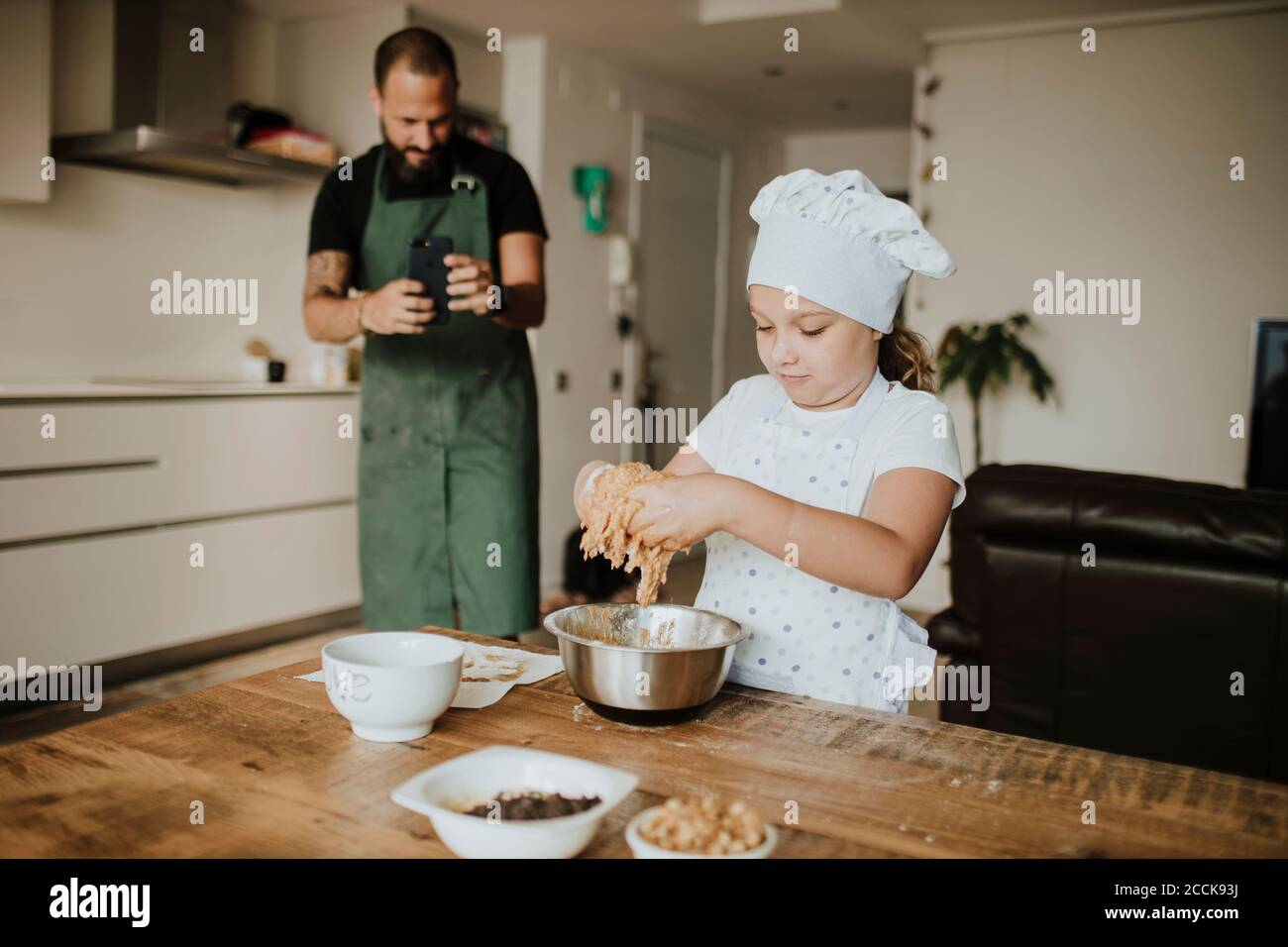 Padre e figlia che stanno facendo cuocere i biscotti a casa, padre che ha scattato una foto con lo smartphone Foto Stock