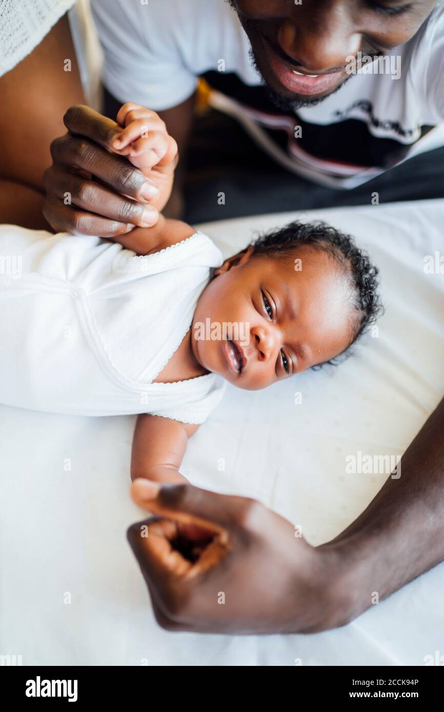 Primo piano dei genitori che tengono le mani della figlia neonato distesi sul letto a casa Foto Stock