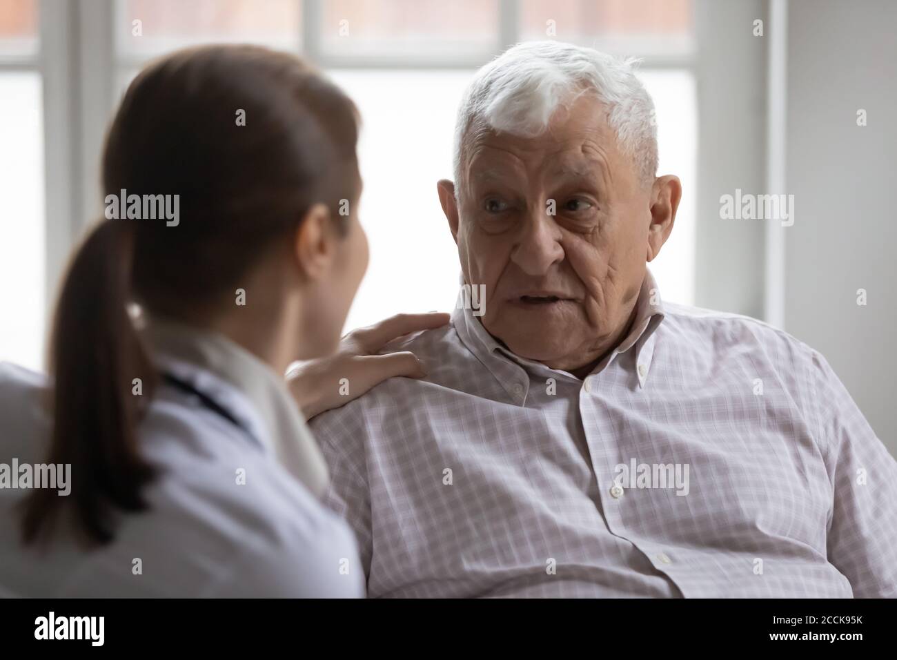 Triste uomo più vecchio degli anni '80 che condivide problemi di salute con l'infermiera giovane. Foto Stock