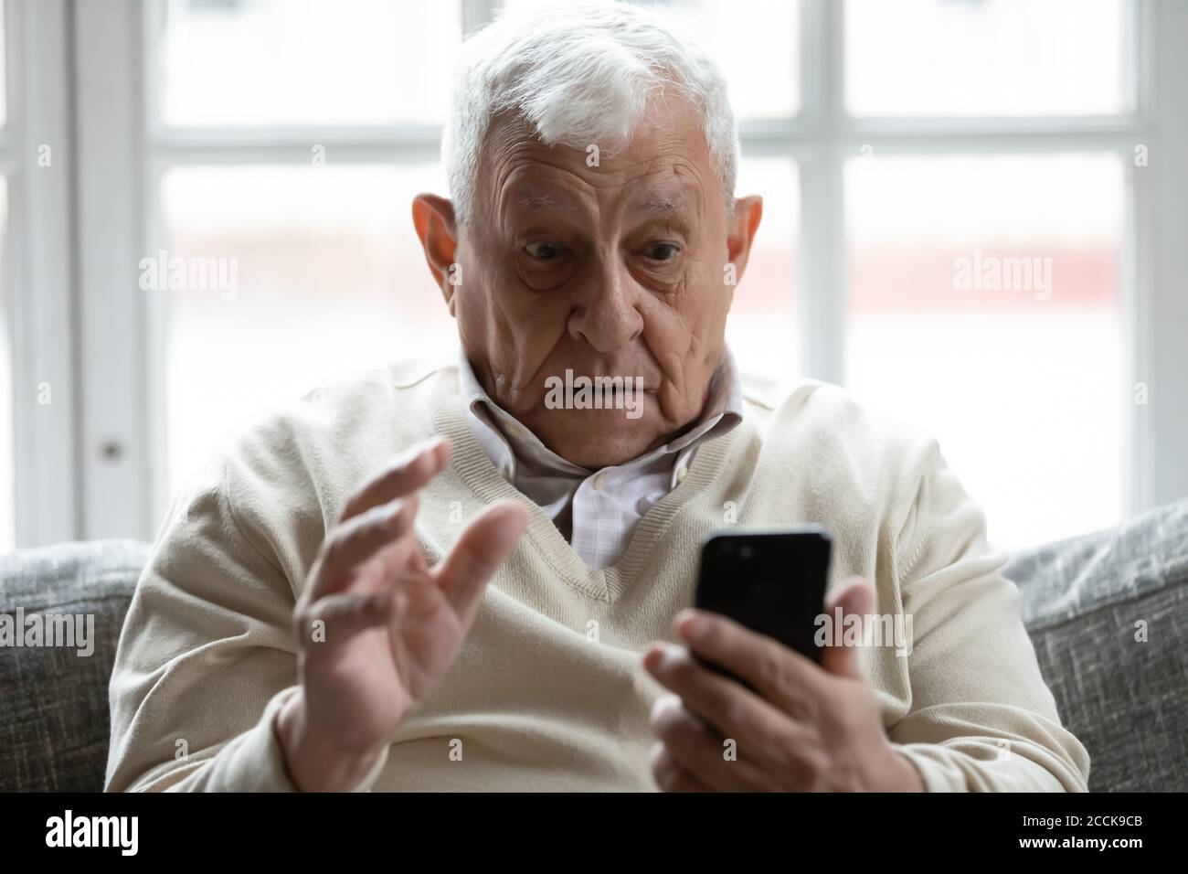 Scioccato anni '70 in pensione vecchio guardando lo schermo dello smartphone. Foto Stock