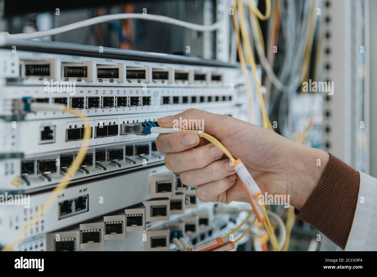 Primo piano di una donna che collega il cavo in fibra ottica all'apparecchiatura a. data center Foto Stock