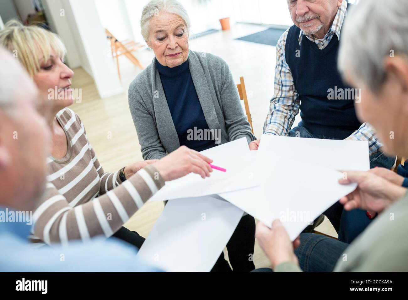 Gruppo di anziani che frequentano il gruppo di terapia in casa di riposo, utilizzando fogli di carta Foto Stock