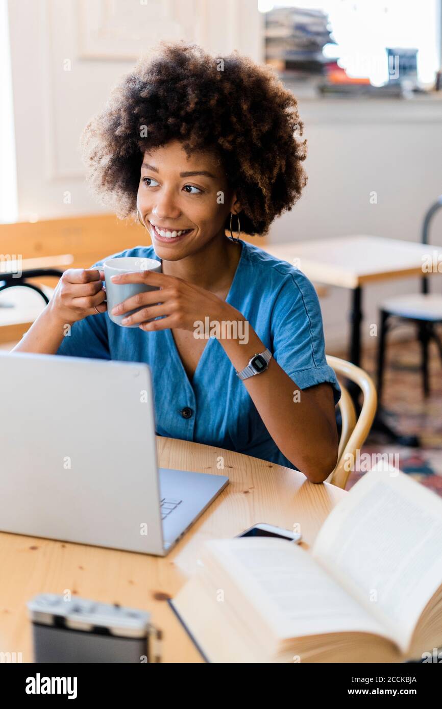 Donna premurosa che tiene la tazza del caffè mentre si siede con il computer portatile a. caffetteria Foto Stock