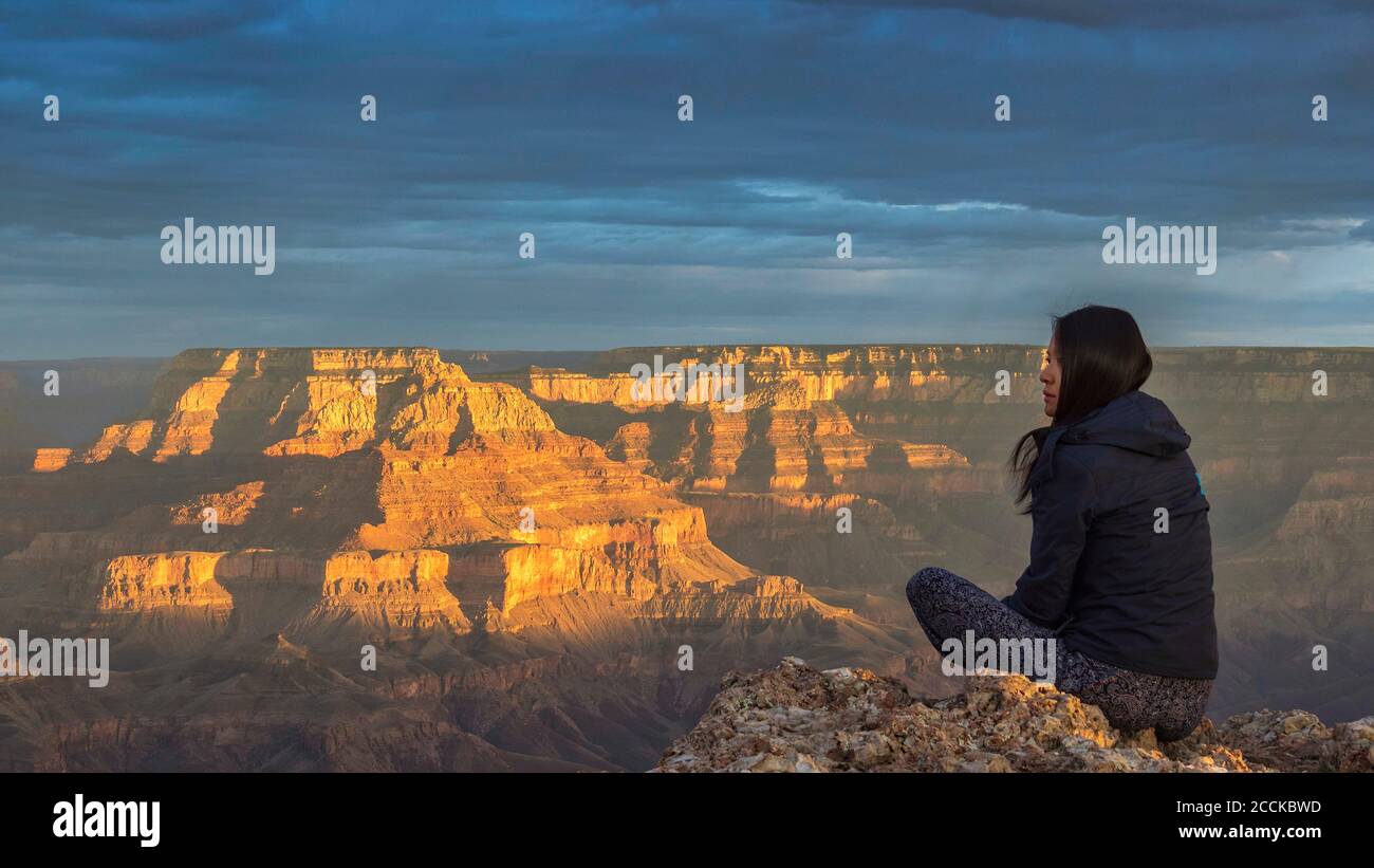 USA, Arizona, vista posteriore della donna seduta sulla roccia al Grand Canyon al tramonto Foto Stock