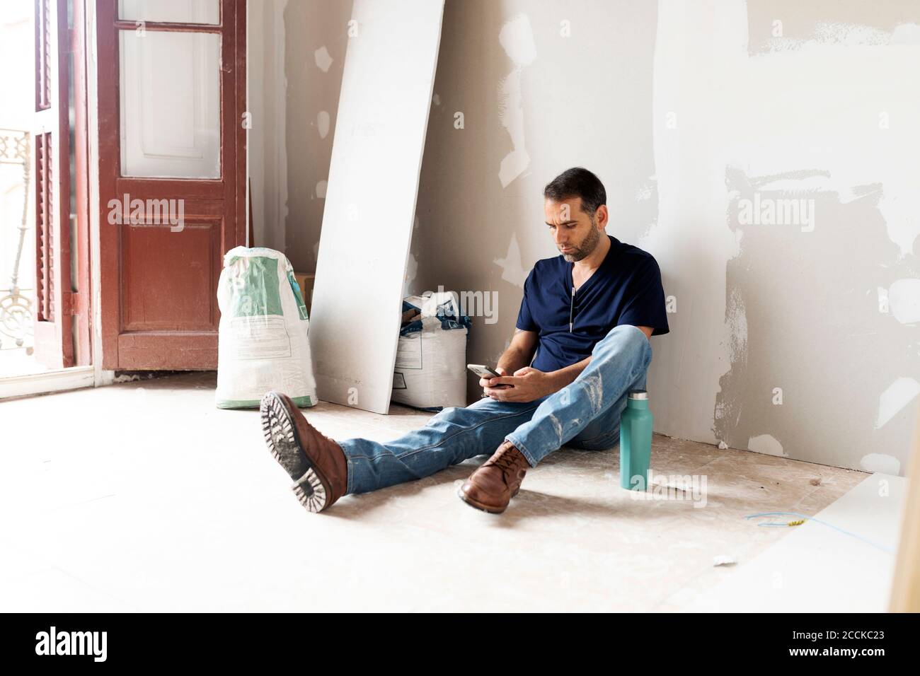 Lavoratore che ha una pausa in una casa in costruzione utilizzando telefono cellulare Foto Stock