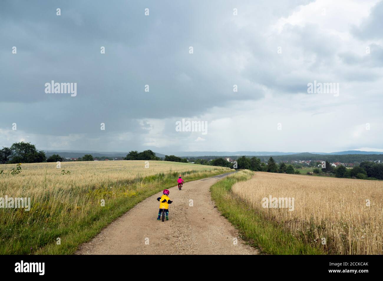 Ragazze con bicicletta e bicicletta in equilibrio su pista sterrata, nuvole di pioggia Foto Stock
