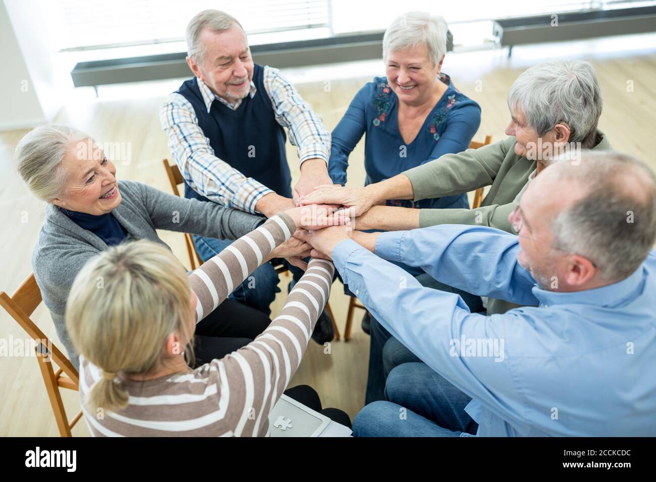 Gruppo di anziani attivi che accatastano le mani, simbolizzando la solidarietà Foto Stock