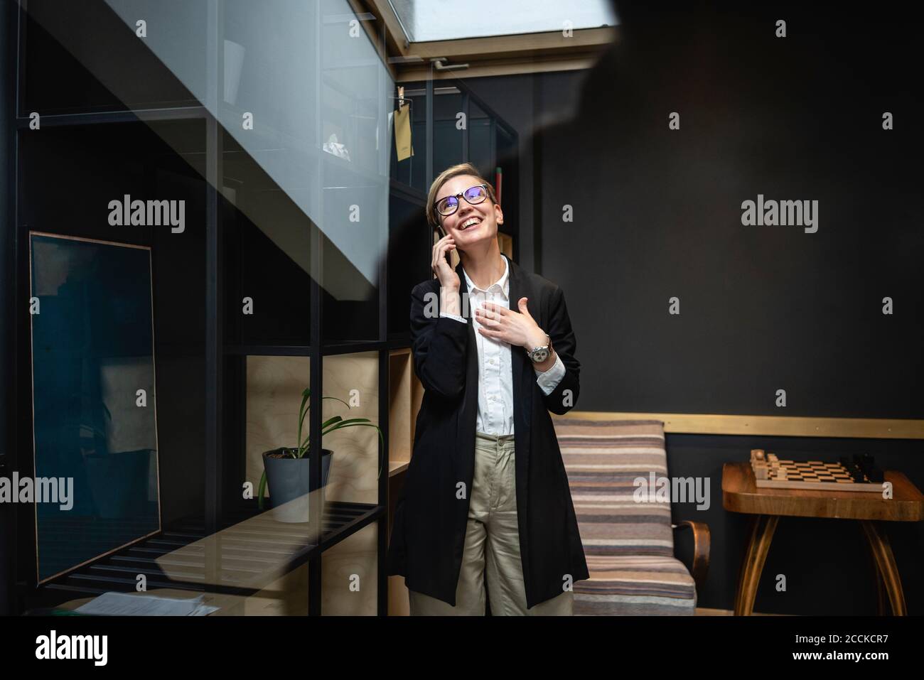 Donna d'affari felice che guarda in su mentre parla con il telefono mobile in ambiente di lavoro creativo Foto Stock