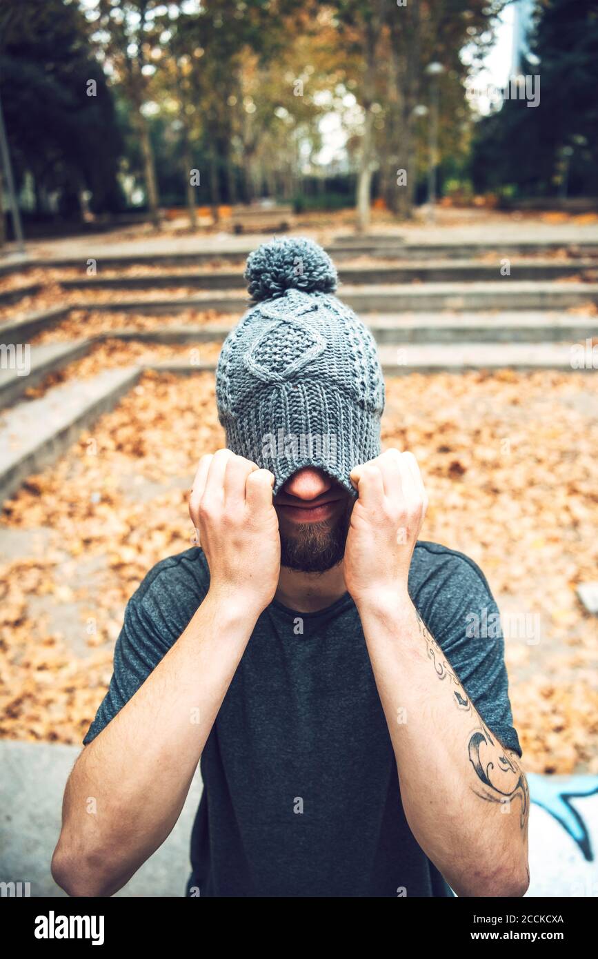 Giovane uomo che copre il viso con cappello a maglia mentre si sta in piedi parco durante l'autunno Foto Stock
