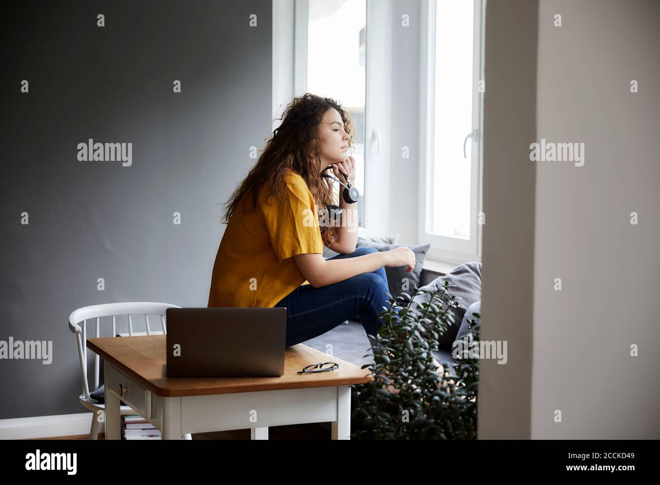 Donna premurosa che guarda attraverso la finestra mentre si prende la pausa dal lavoro in soggiorno presso l'ufficio di casa Foto Stock