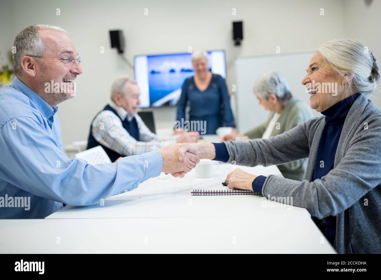 Gli anziani si riuniscono al corso di miglioramento delle competenze, scuotendo le mani Foto Stock