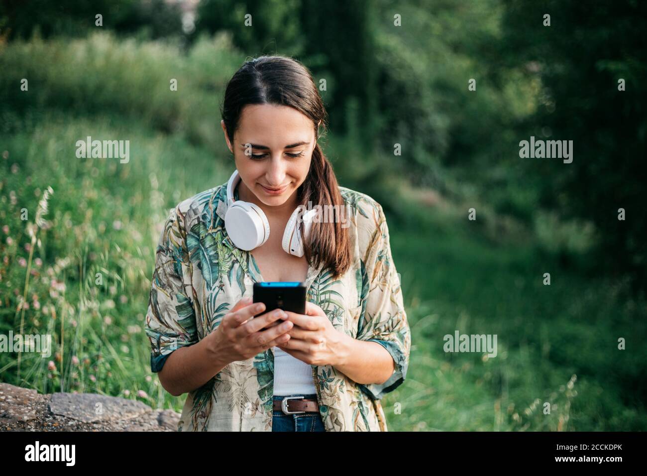 Messaggi sorridenti da parte di una donna dallo smartphone al parcheggio Foto Stock