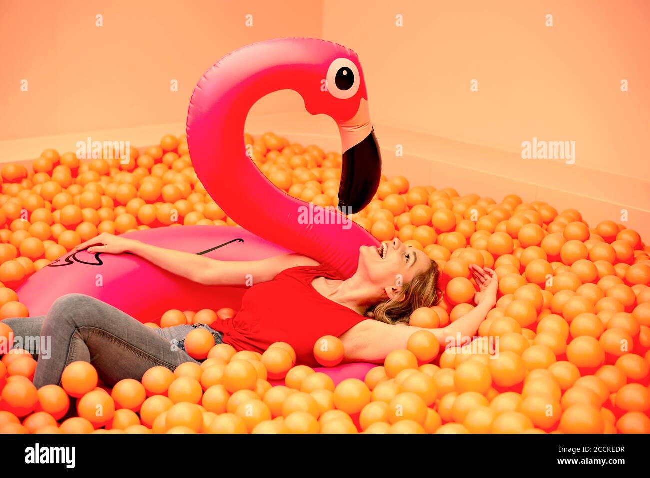 Giovane donna allegra con fenicottero gonfiabile sdraiato in palla arancione buca Foto Stock