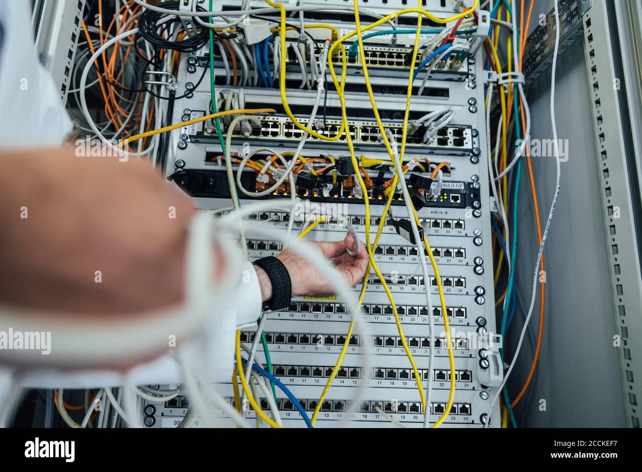 Primo piano del cavo di collegamento uomo a mano maturo nel data center rack Foto Stock