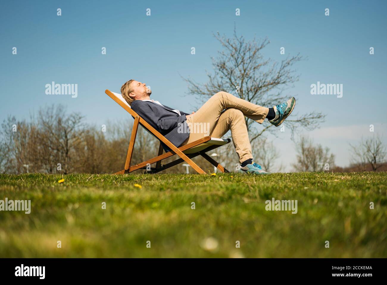 Vista a livello della superficie di un uomo d'affari che si rilassa sulla sedia del parco durante il giorno di sole Foto Stock