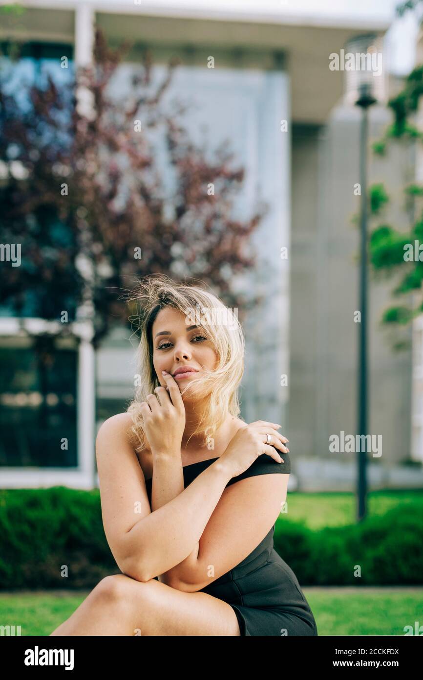 Giovane donna che indossa un abito nero seduto al parco in città Foto Stock