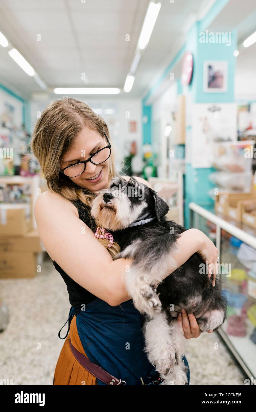 Buon groomer femmina abbracciando schnauzer mentre si trova in piedi in salone per animali domestici Foto Stock