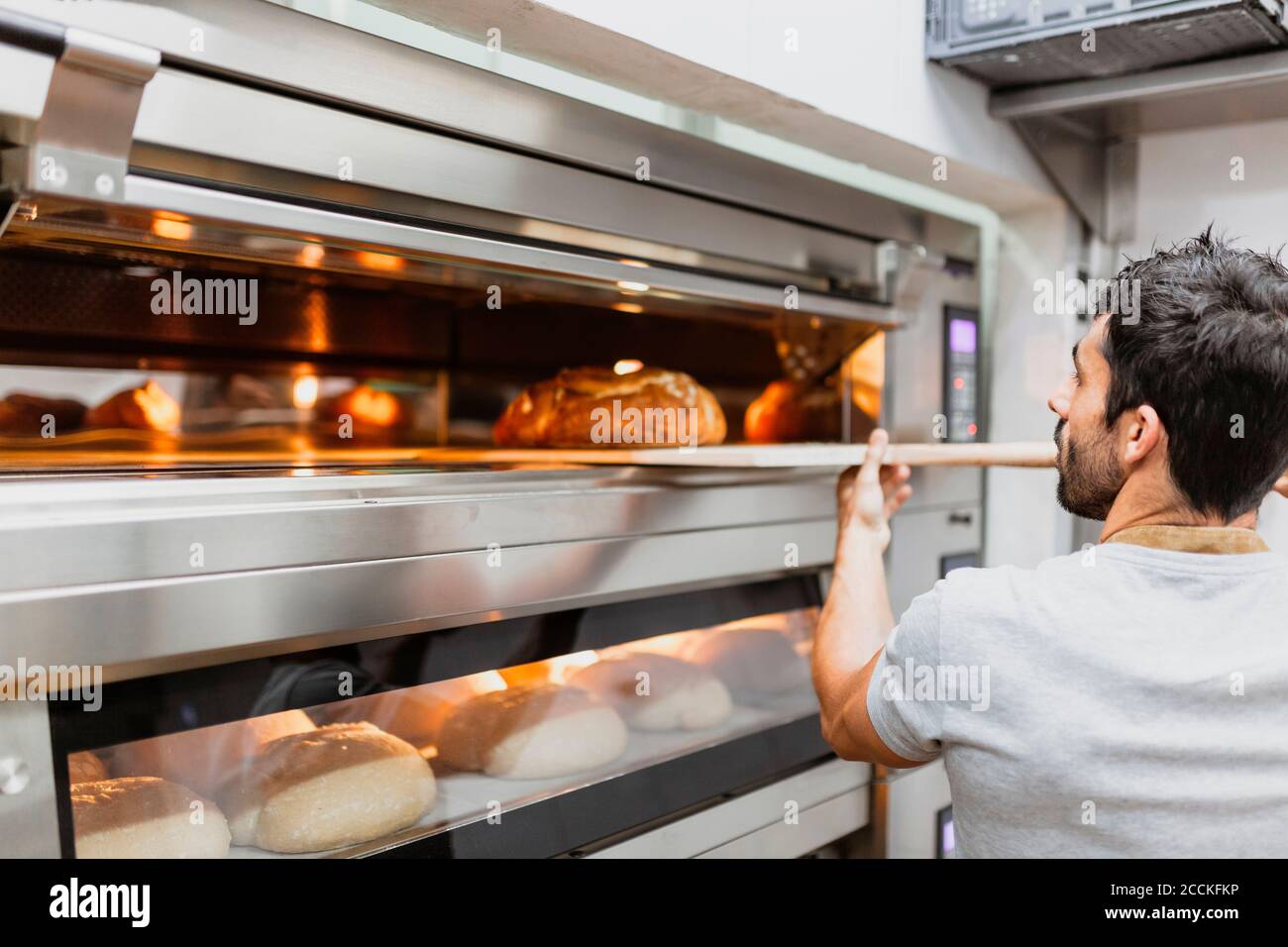 Panettiere che cuoce il pane nel forno al forno Foto Stock