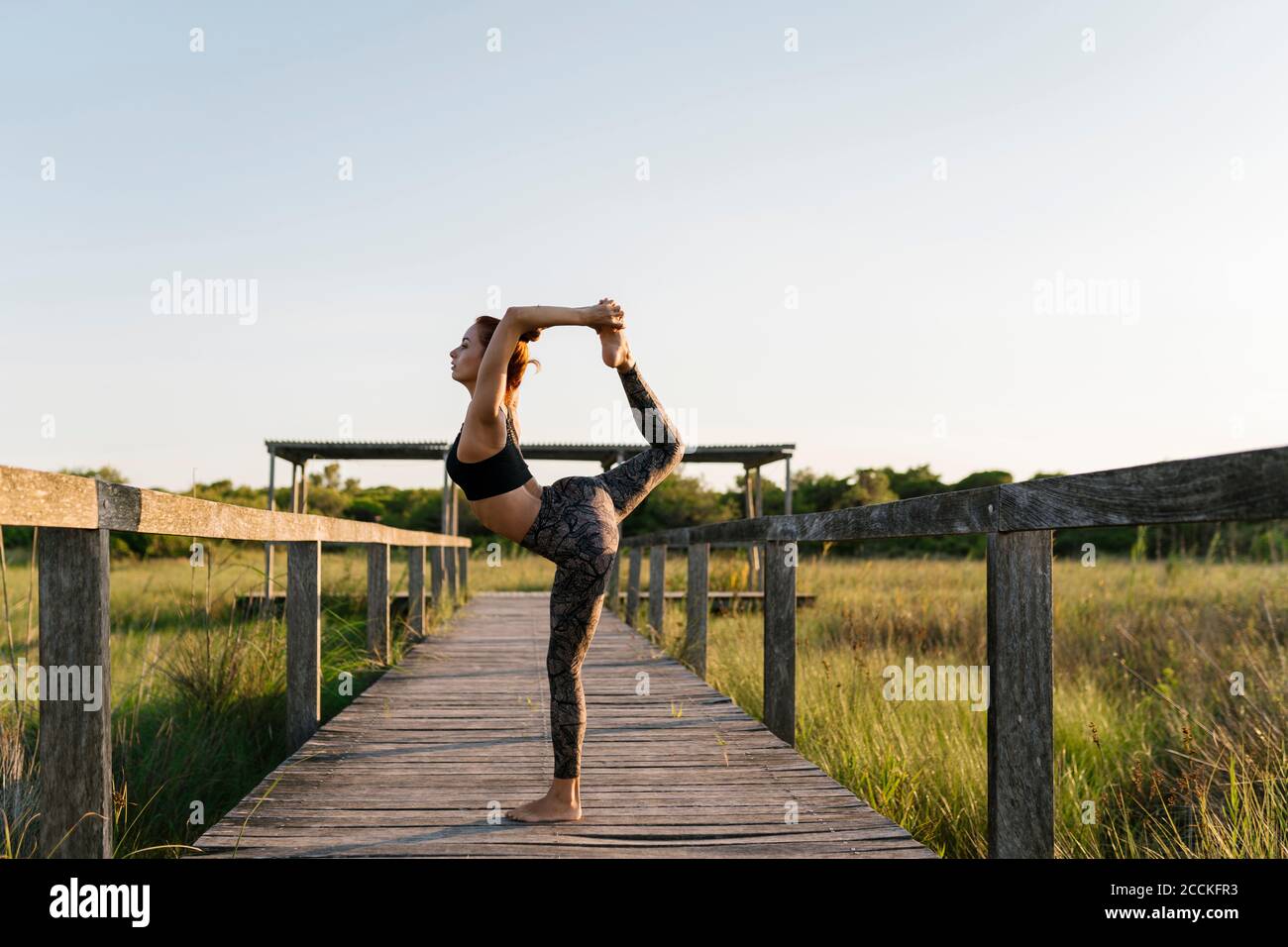 Donna che pratica yoga mentre si trova sul molo in campagna Foto Stock