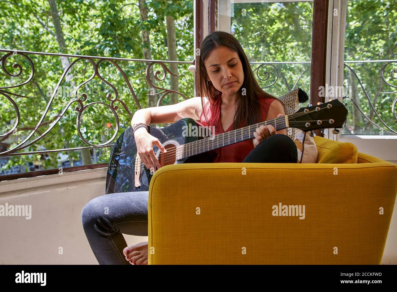 Donna che suona la chitarra mentre si siede sulla sedia nel balcone Foto Stock