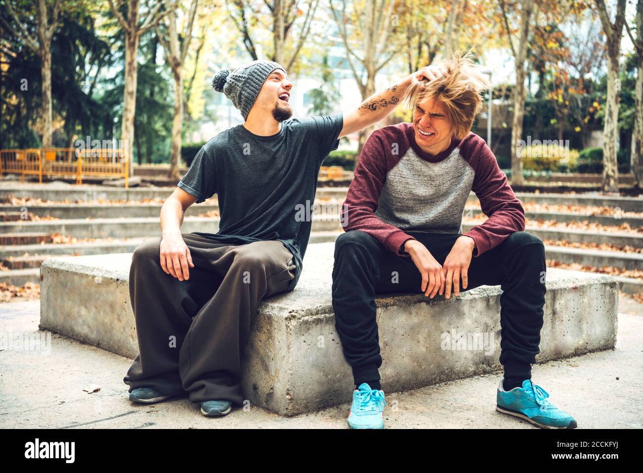 Sorridente maschio che guarda i capelli dell'amico mentre si siede nel parco pubblico Foto Stock