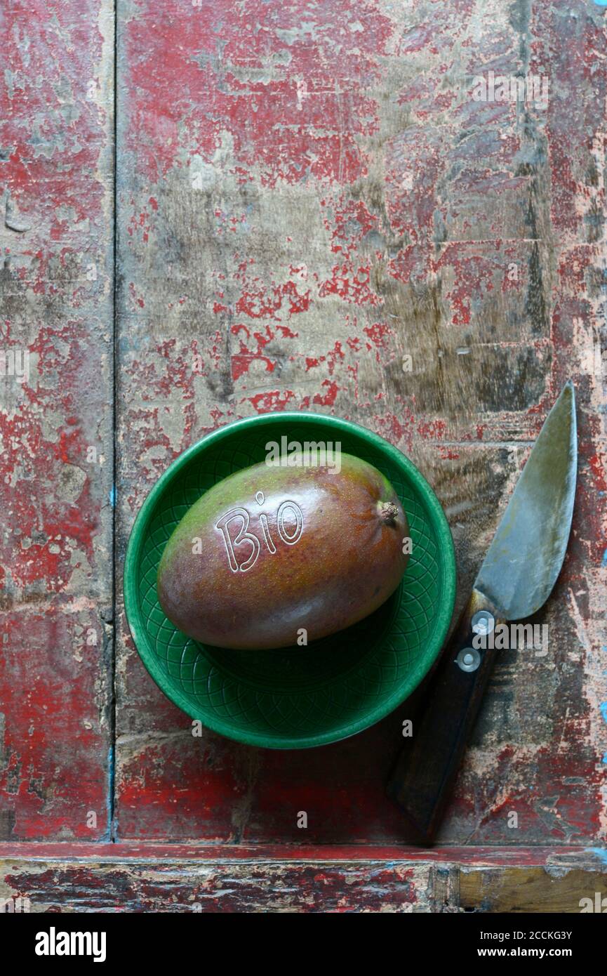 Piccola ciotola, frutta di mango e coltello da cucina adagiato su una superficie di legno intemperie Foto Stock