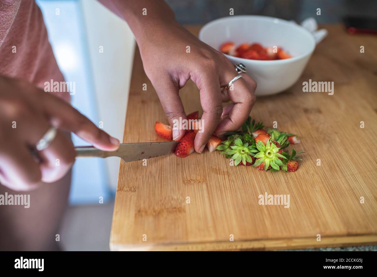 Primo piano di una giovane donna che trita fragole sul tagliere cucina a casa Foto Stock