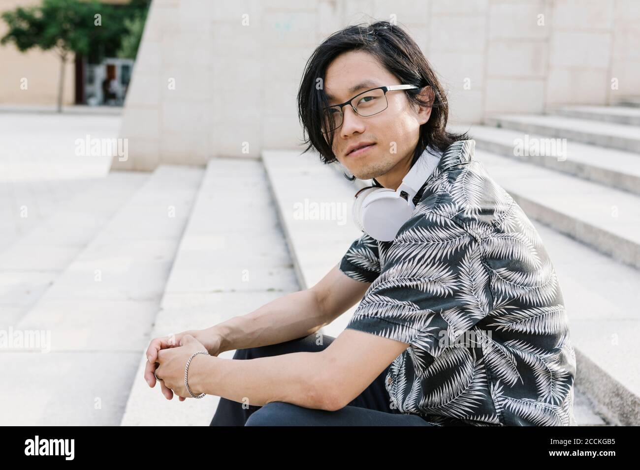 Giovane uomo che indossa gli occhiali con le cuffie seduti sui gradini città Foto Stock
