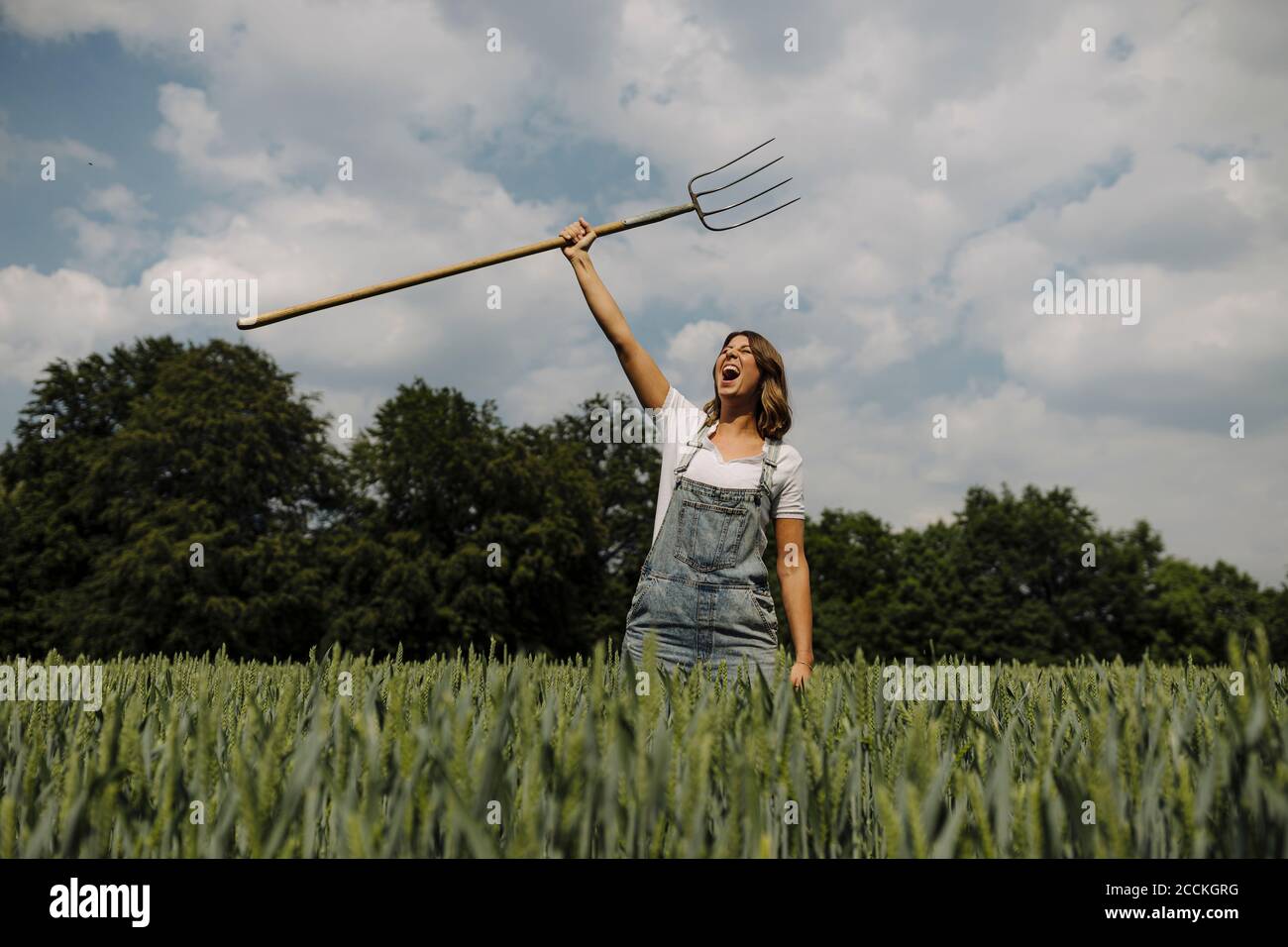 Urlando giovane donna che solleva la forchetta di fieno in un grano campo in campagna Foto Stock