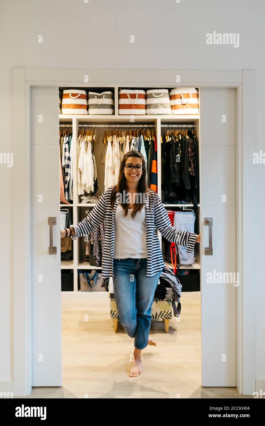 Giovane donna sorridente che apre le porte dello spogliatoio a casa Foto Stock