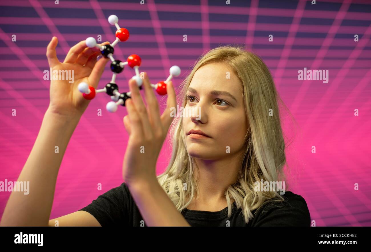 Primo piano di una scienziata femminile che tiene il modello di molecola contro il modello di griglia Foto Stock