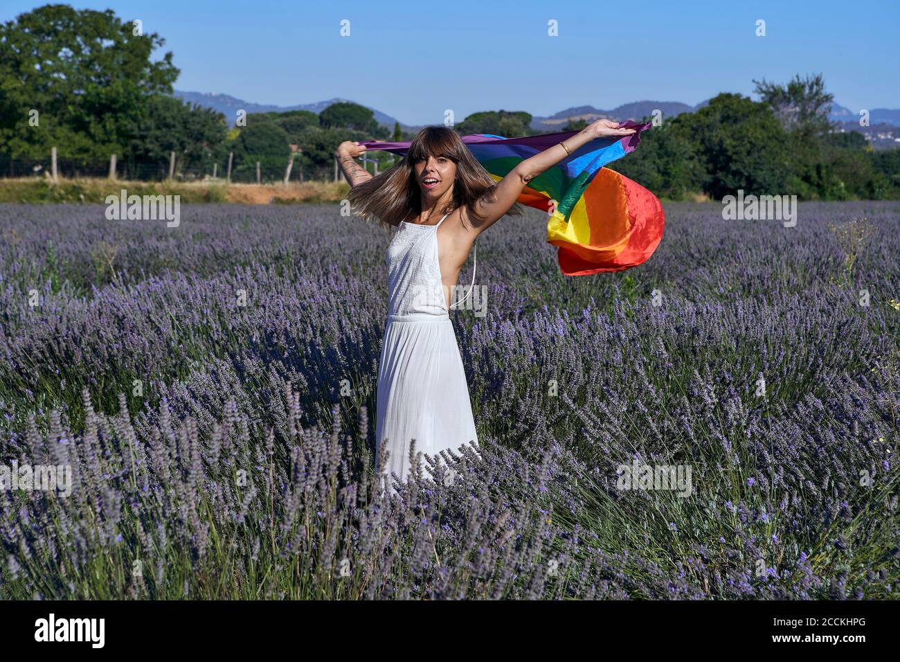 Donna mid adult con bandiera arcobaleno in piedi in mezzo alla lavanda campo Foto Stock
