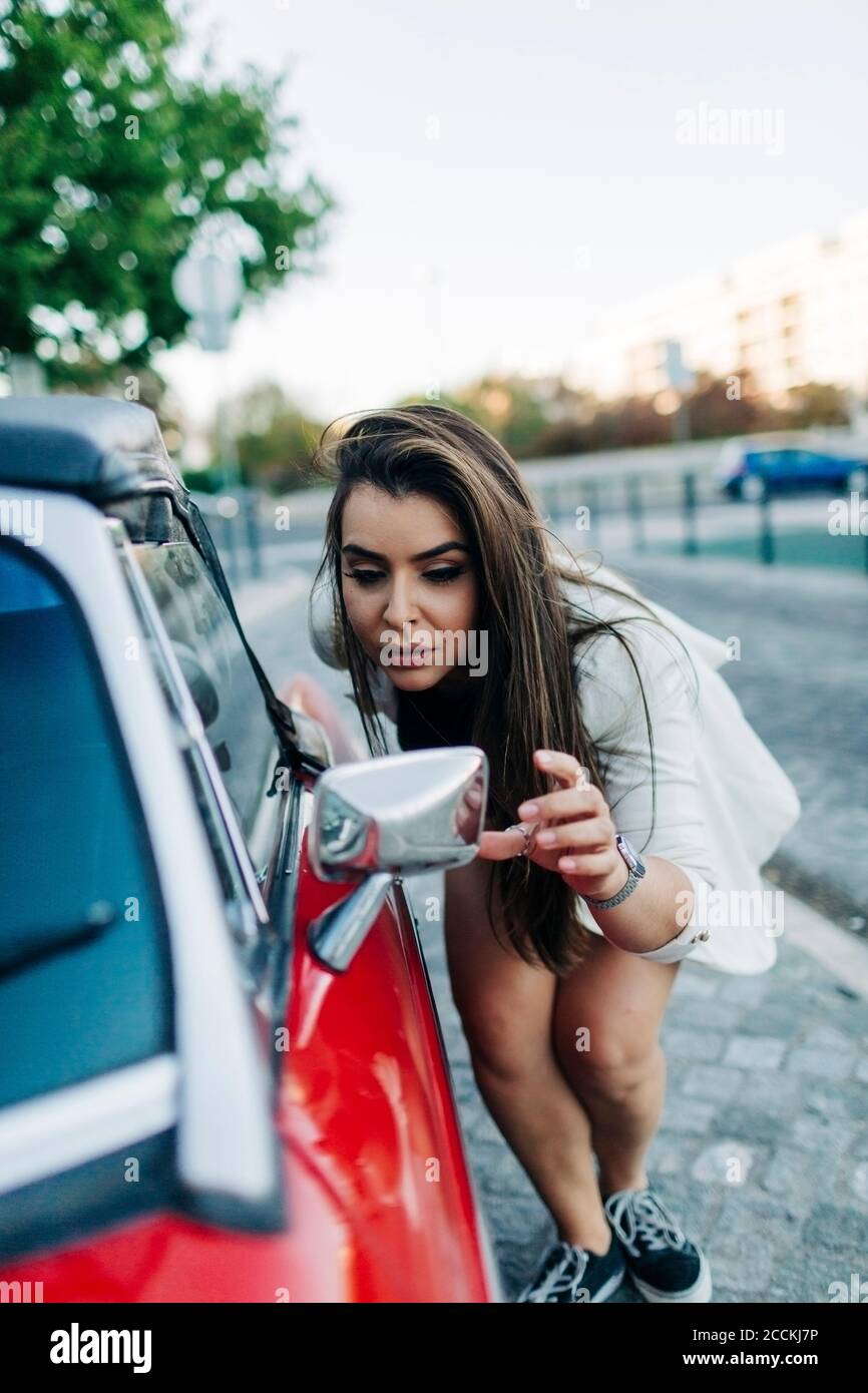 Giovane donna che controlla il suo sguardo nello specchio dell'automobile Foto Stock