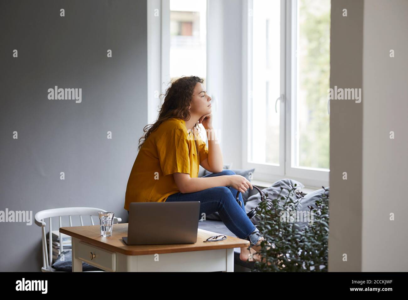 Donna premurosa con mano sul mento guardando attraverso la finestra mentre prendere la pausa dal lavoro in salotto in ufficio domestico Foto Stock