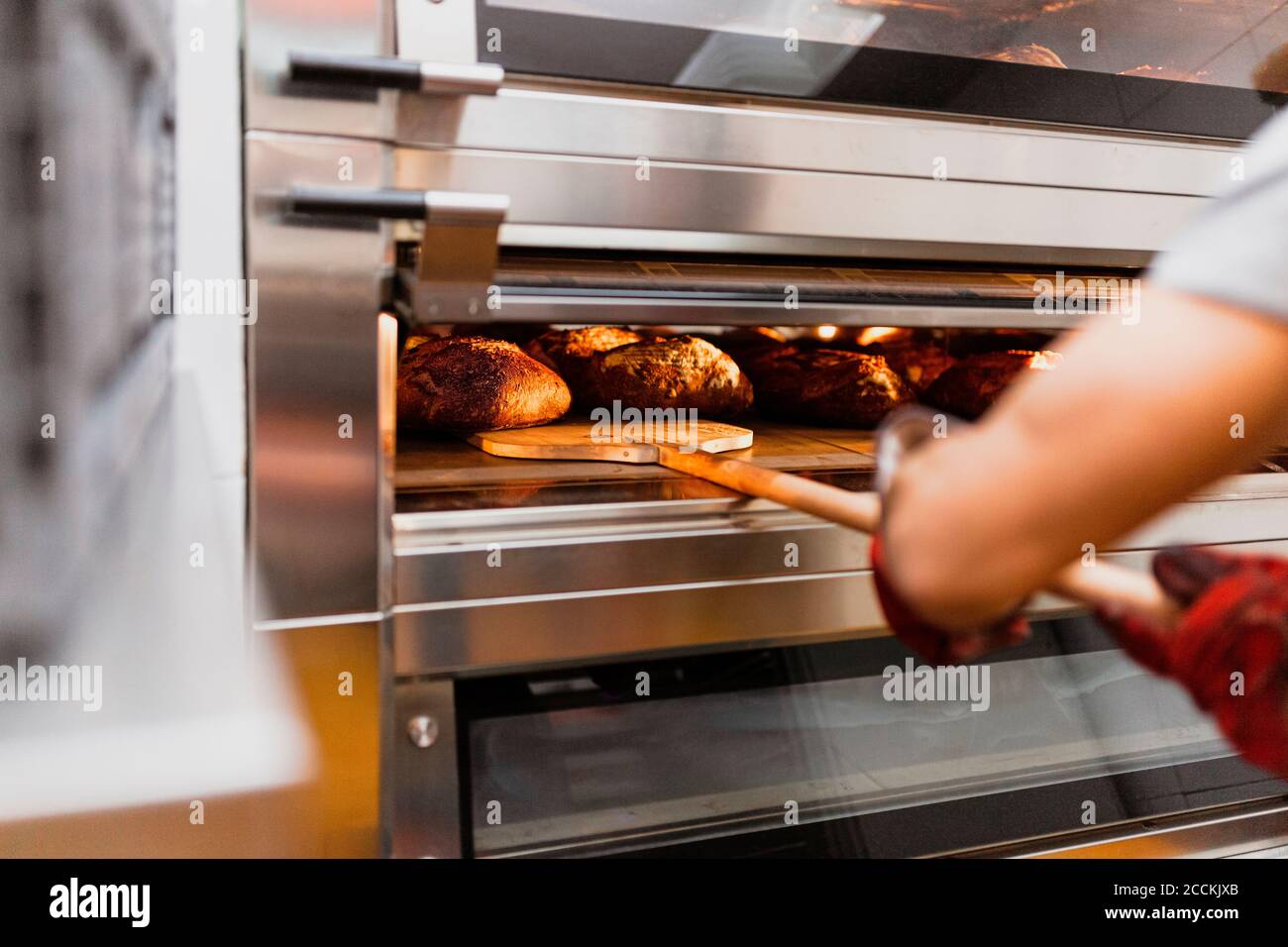 Mano tagliata di panettiere maschio che cuoce il pane in forno a. panificio Foto Stock