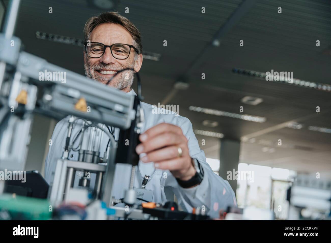 Uomo sorridente e maturo che indossa occhiali e attrezzature per l'esame in laboratorio Foto Stock