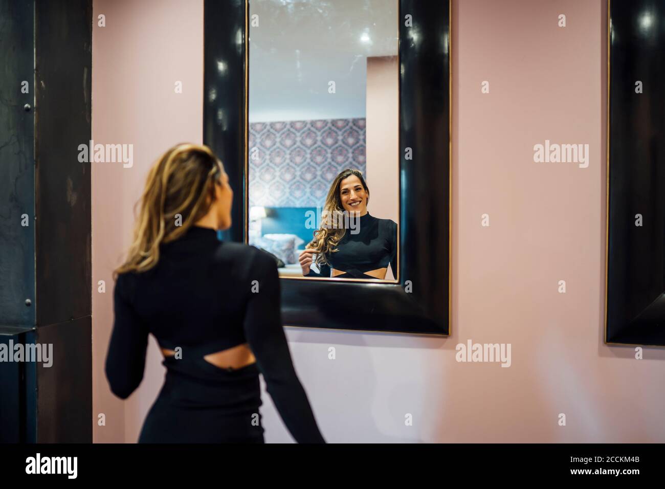 Donna mid adulta sorridente che indossa un abito che guarda nello specchio località turistica Foto Stock