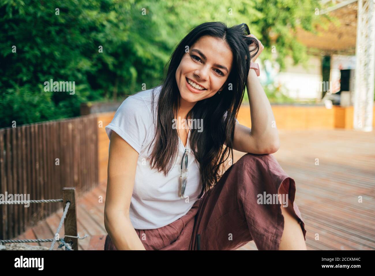 Sorridente bella donna con la mano in capelli seduta al parco Foto Stock